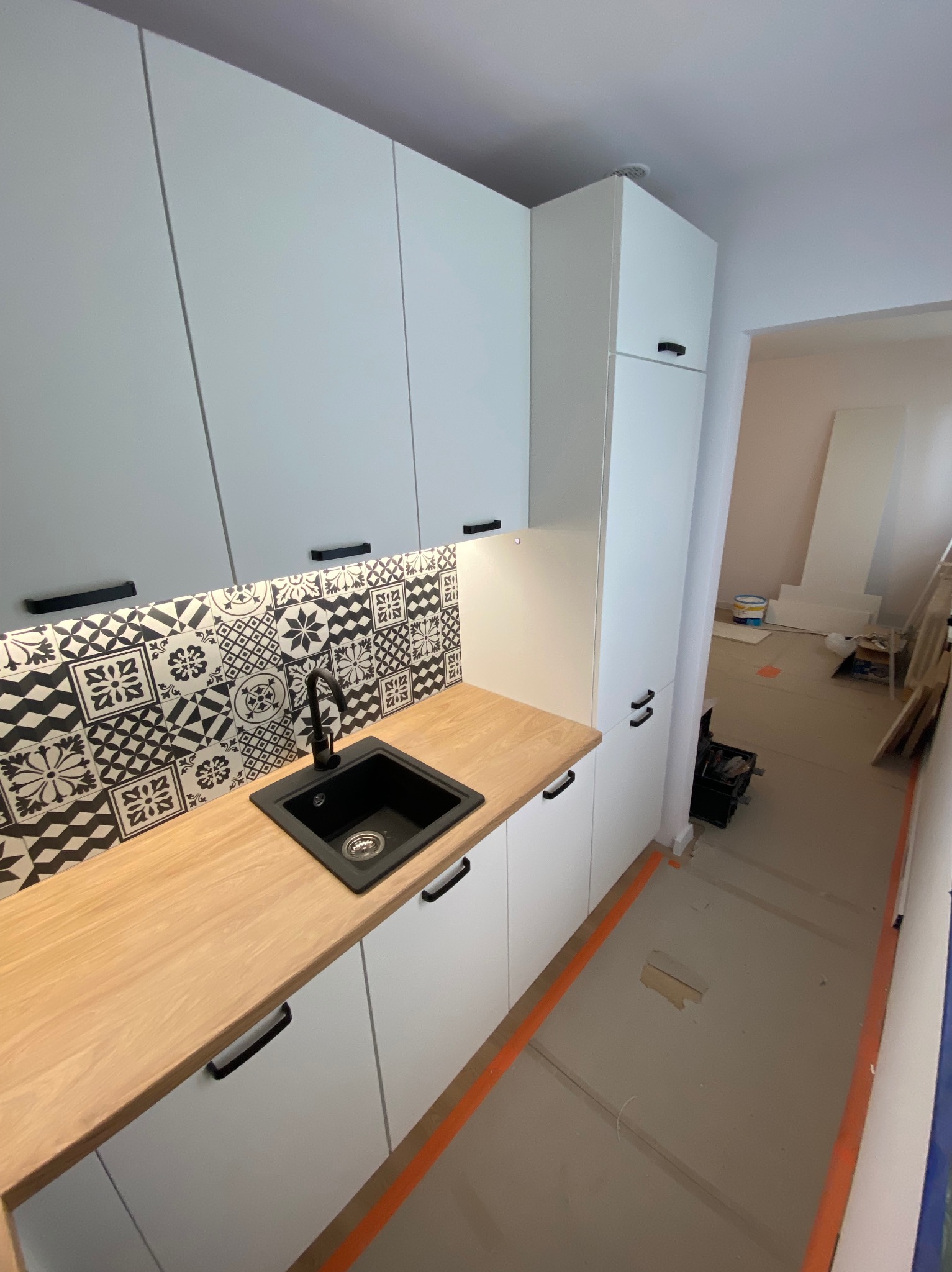 Nowoczesna kuchnia z białymi szafkami i drewnianym blatem w Starowej Górze. Uwagę przykuwają czarne, wzorzyste płytki nad blatem i czarny zlew.