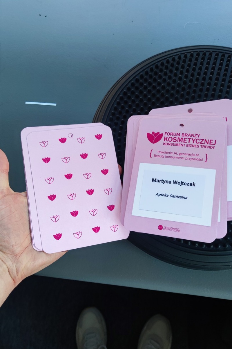 Różowe identyfikatory z logo i napisem 'Forum Branży Kosmetycznej' leżące na czarnym tle, w dłoni.