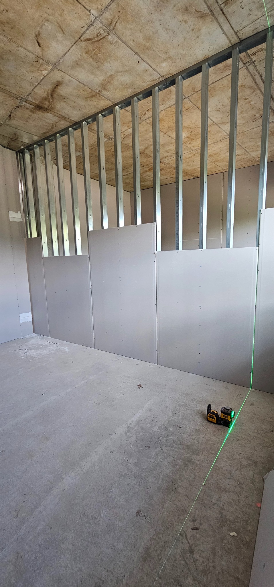 Montaż płyt gipsowo-kartonowych na metalowym stelażu, widoczny laser krzyżowy wyznaczający poziom. Surowy stan, przygotowanie do dalszych prac wykończeniowych.