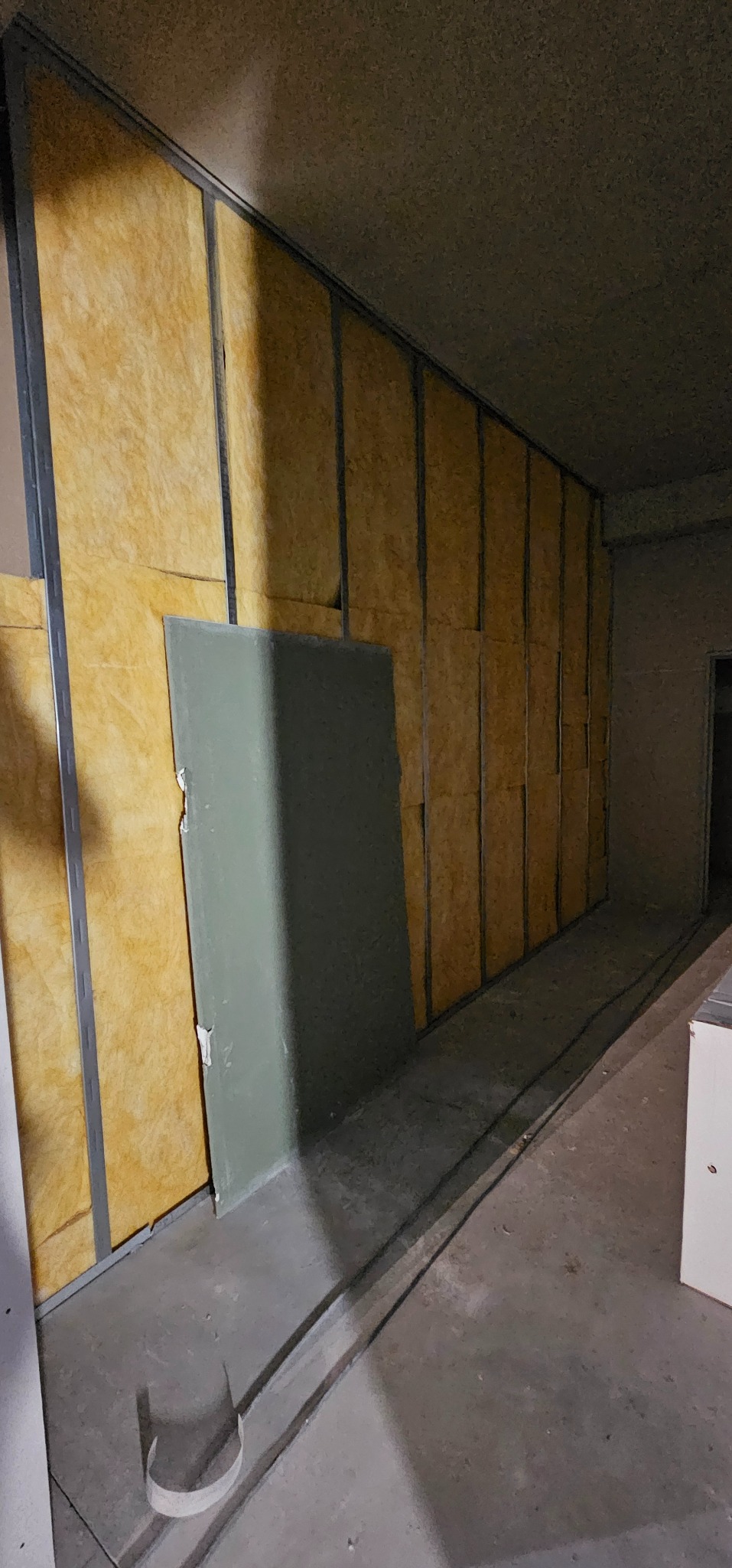 Ściana w trakcie wykańczania: metalowy stelaż z izolacją z wełny mineralnej. Częściowo zamontowana płyta karton-gips, widoczne łączenia. Surowy stan podłogi.