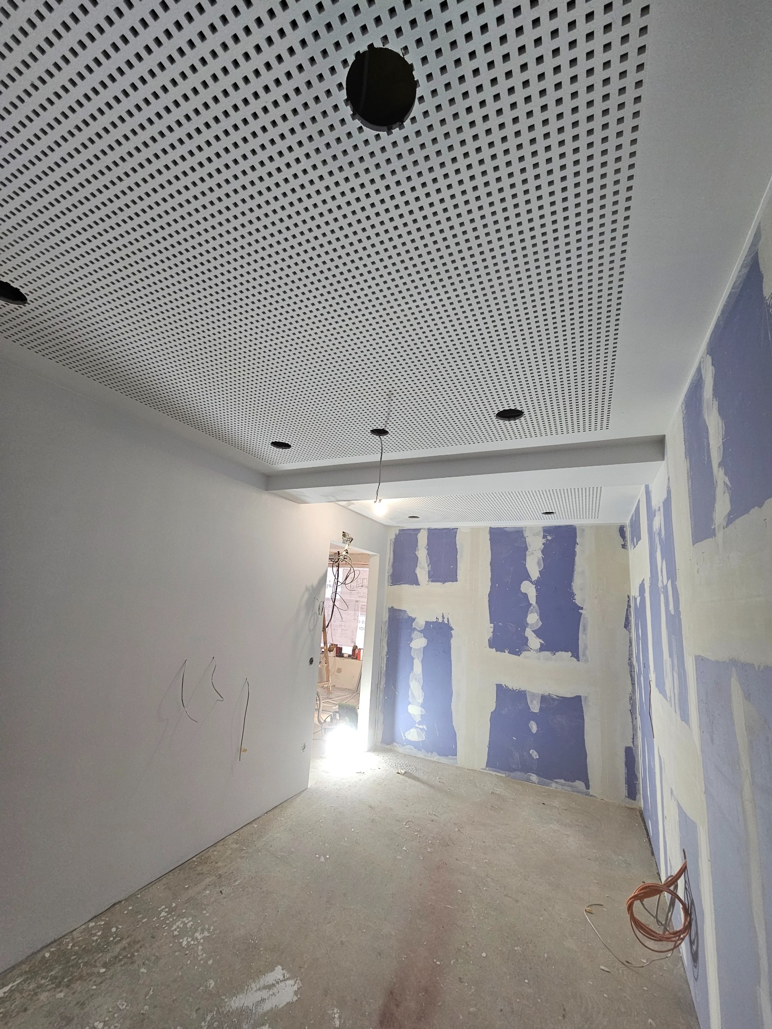 Sufit z perforowanej płyty karton-gips w trakcie montażu, widoczne przygotowane ściany do szpachlowania i wystające przewody. Otwory na oświetlenie.