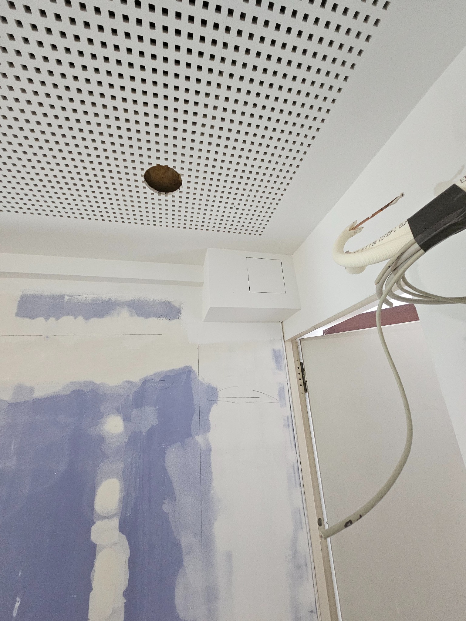 Sufit z perforowanej płyty w Słupsku, ściana w trakcie szpachlowania, widoczne przewody. Prace wykończeniowe w pomieszczeniu.