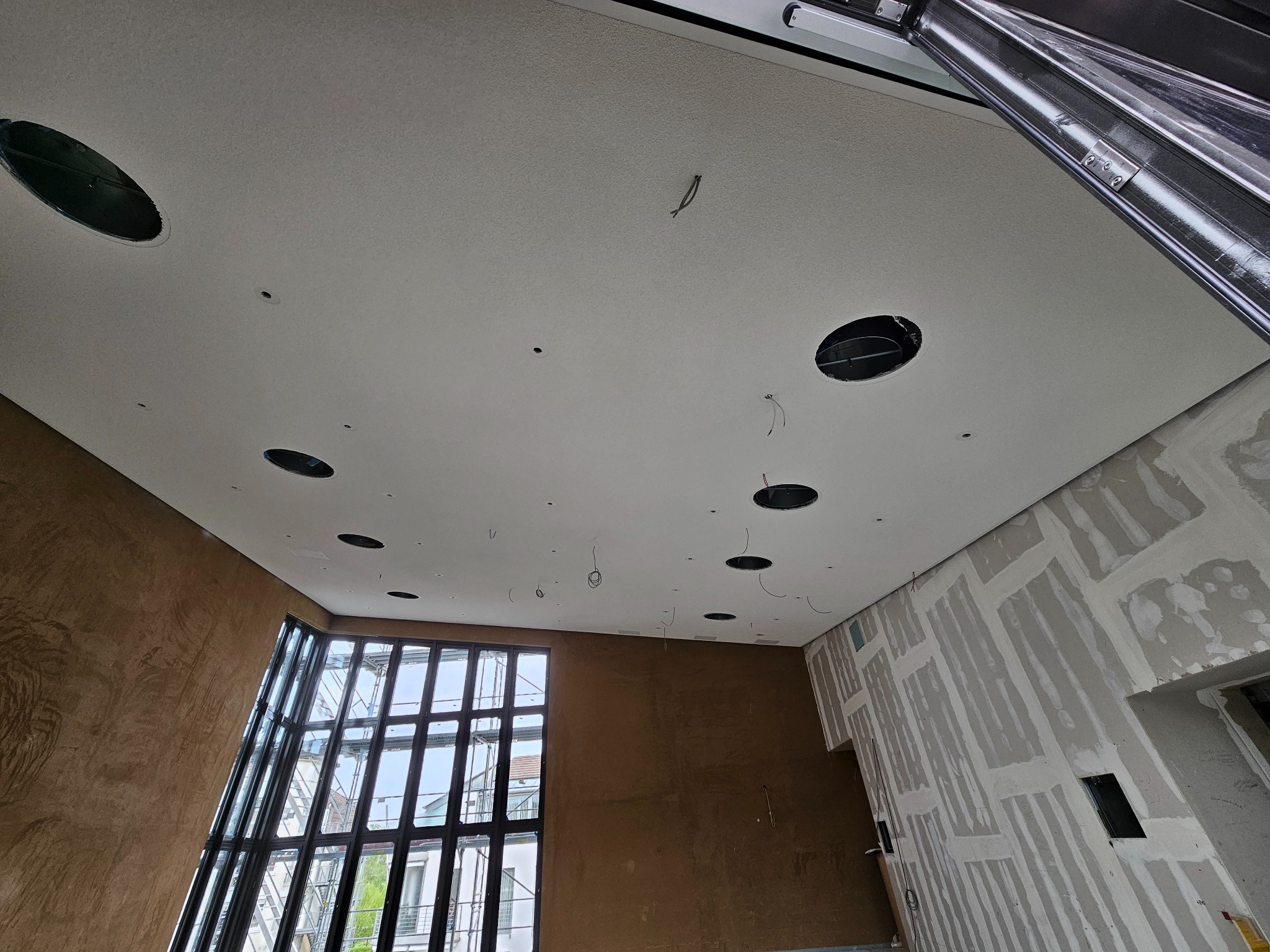 Sufit z płyt karton-gips z otworami na oświetlenie, ściana z fakturą i okno z widokiem na zewnątrz. Prace wykończeniowe w nowoczesnym wnętrzu.