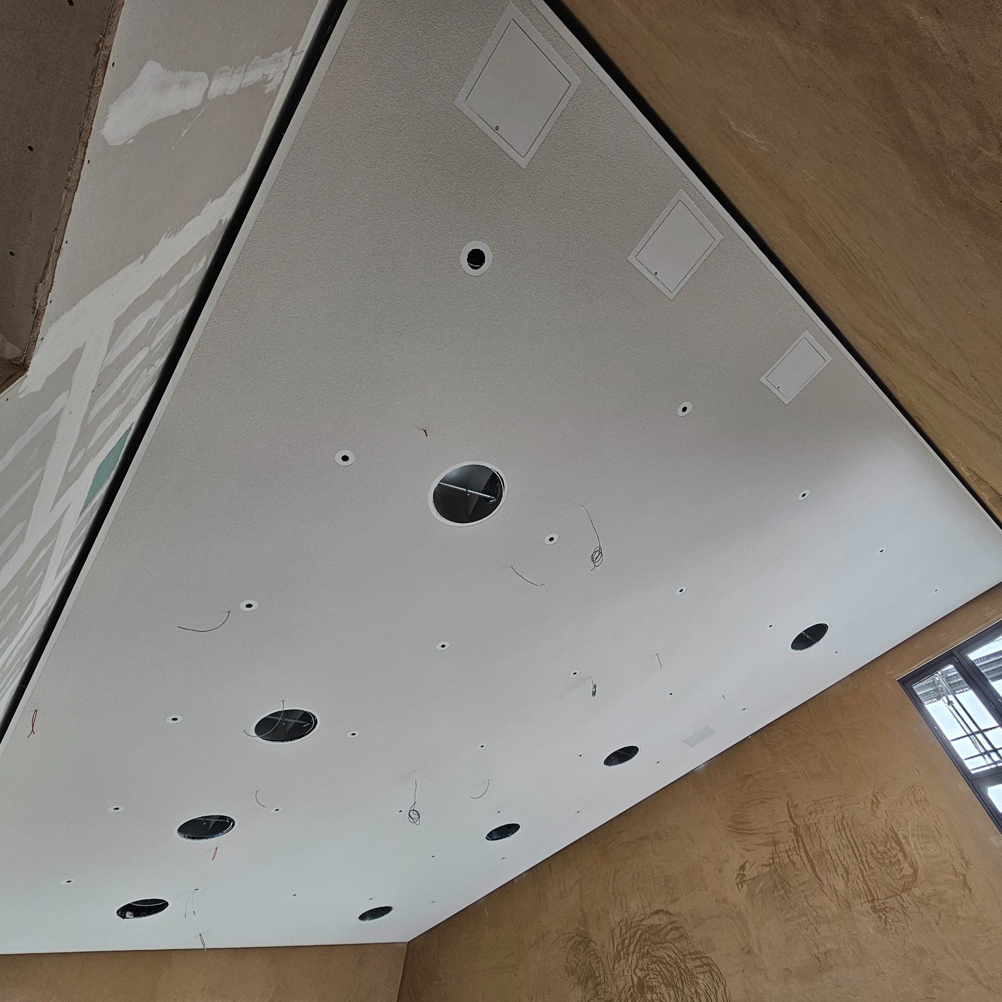 Wykończony sufit podwieszany z płyty gipsowej w biurze, z widocznymi otworami na oświetlenie i panelami dostępowymi. Dekoracyjna faktura ściany w tle.