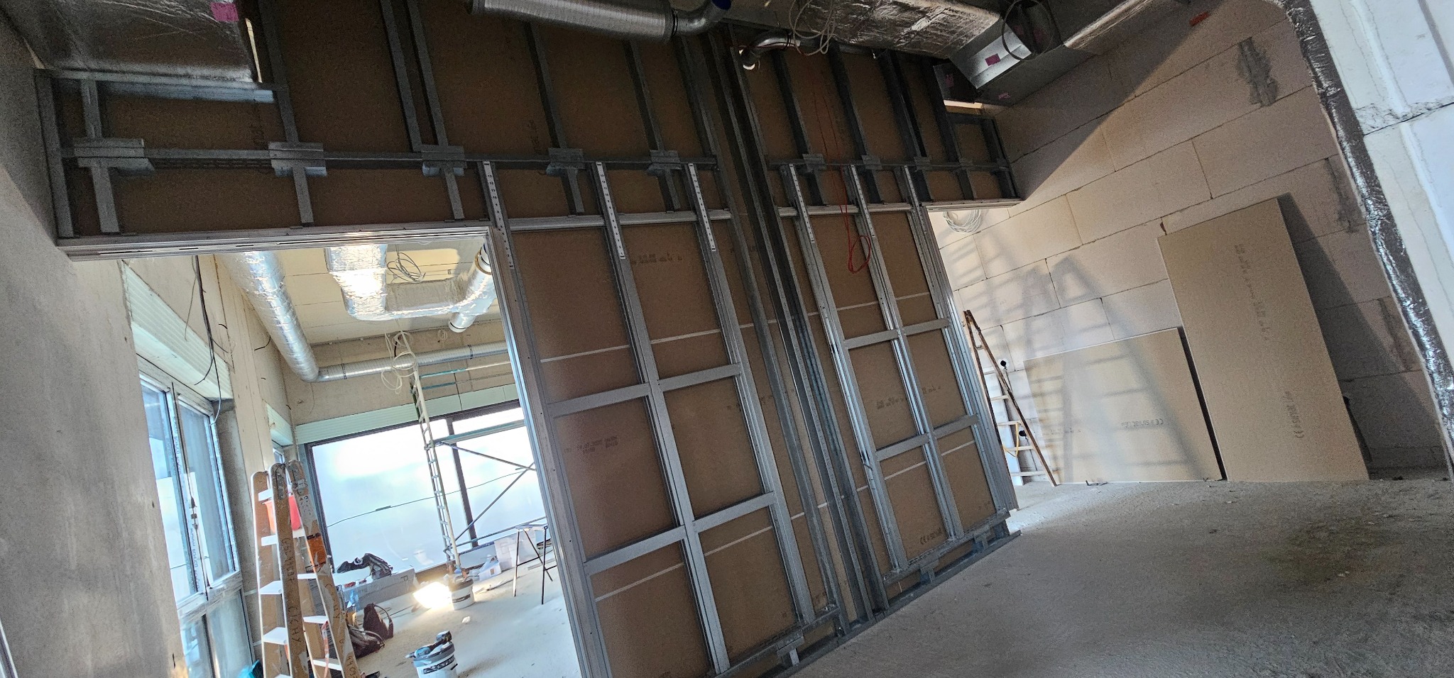 Metalowa konstrukcja pod płyty kartonowo-gipsowe, widoczne instalacje wentylacyjne pod sufitem, surowe ściany z bloczków. Prace wykończeniowe w biurze.