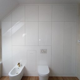 EdiMeb Meble na wymiar - Biała, lakierowana szafa wnękowa pod skosem w łazience, z ukrytą spłuczką WC i bidetem. Złota armatura. Drewnopodobna podłoga. Minimalistyczny design.