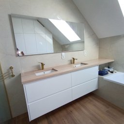 EdiMeb Meble na wymiar - Nowoczesna łazienka na poddaszu z dwiema umywalkami nablatowymi i drewnianym blatem. W lustrze odbija się biała szafa w skosie. Złota armatura i drewnopodobna podłoga.