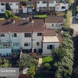 Urban Prism Media - Zdjęcie z drona przedstawia osiedle domów jednorodzinnych z zadbanymi ogrodami. Widoczny kamper i samochody na podjazdach. Tło: zielone drzewa i krzewy.