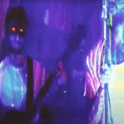 Urban Prism Media - Ujęcie z teledysku w Jeleniej Górze: dwaj muzycy w neonowym oświetleniu, jeden z gitarą, drugi w jasnej koszulce. Dynamiczna scena z koncertu.