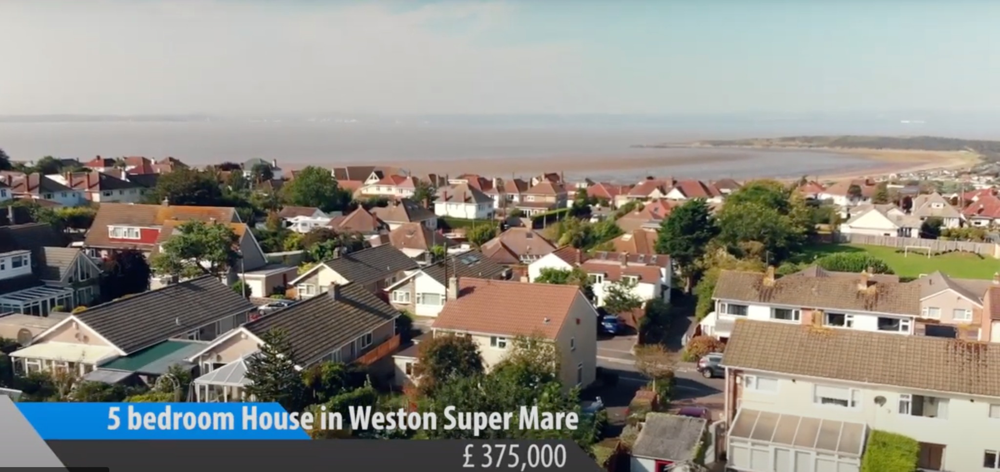 Panoramiczny widok z drona na osiedle domów jednorodzinnych w Weston Super Mare, z widoczną linią brzegową w tle i informacją o cenie nieruchomości.