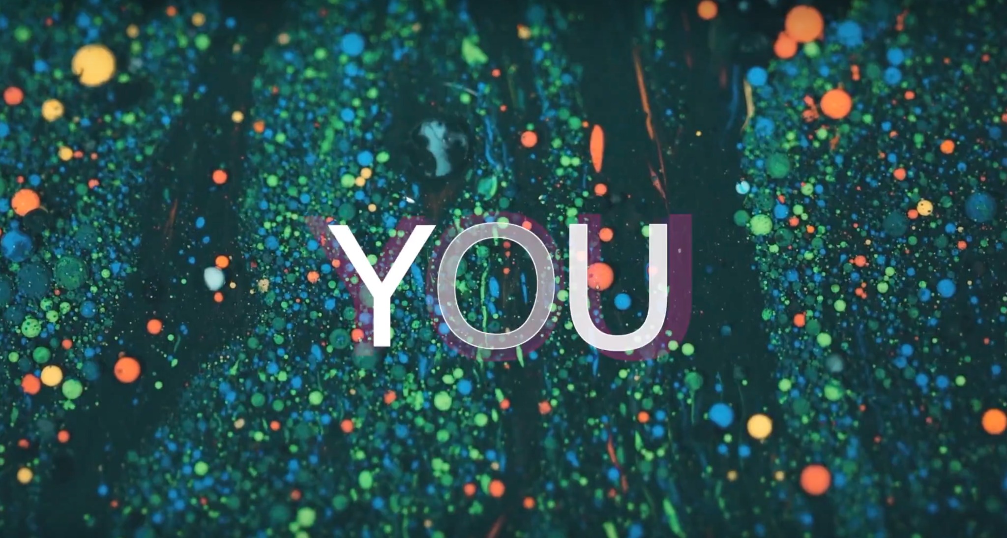 Abstrakcyjna grafika z napisem 'YOU' na tle ciemnego, wzorzystego tła z kolorowymi kropkami i smugami, przypominająca malarską teksturę.