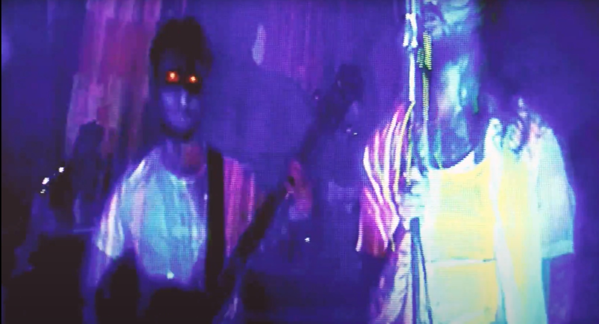 Ujęcie z teledysku w Jeleniej Górze: dwaj muzycy w neonowym oświetleniu, jeden z gitarą, drugi w jasnej koszulce. Dynamiczna scena z koncertu.