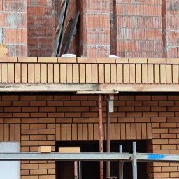 Klinkier -BAU - Murowana elewacja budynku w trakcie budowy, widoczne rusztowania i cegły klinkierowe. Częściowo ocieplony fragment ściany.
