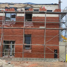 Klinkier -BAU - Budowa domu z cegły: wznoszenie dwukondygnacyjnej elewacji z czerwonej cegły, widoczne rusztowania i materiały budowlane wokół placu budowy.