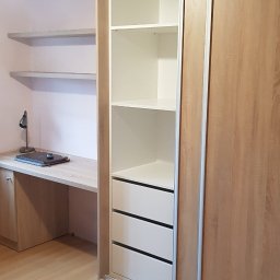 Paweł Zapasek - Szafa na wymiar z przesuwnymi drzwiami w odcieniach drewna, zintegrowana z biurkiem i półkami. Widoczne białe półki i szuflady wewnątrz szafy.