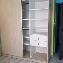 Paweł Zapasek - Otwarta szafa wnękowa z przesuwnymi drzwiami, z półkami i szufladami w Sokołowie Małopolskim. Jasne drewno na drzwiach, białe wnętrze i panele na podłodze.