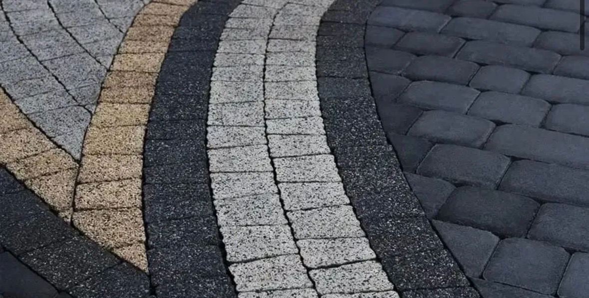 Wzorzyste ułożenie kostki brukowej w odcieniach szarości, brązu i czerni, tworzące dekoracyjny, łukowaty wzór. Bliski kadr, wyraźna faktura materiału.