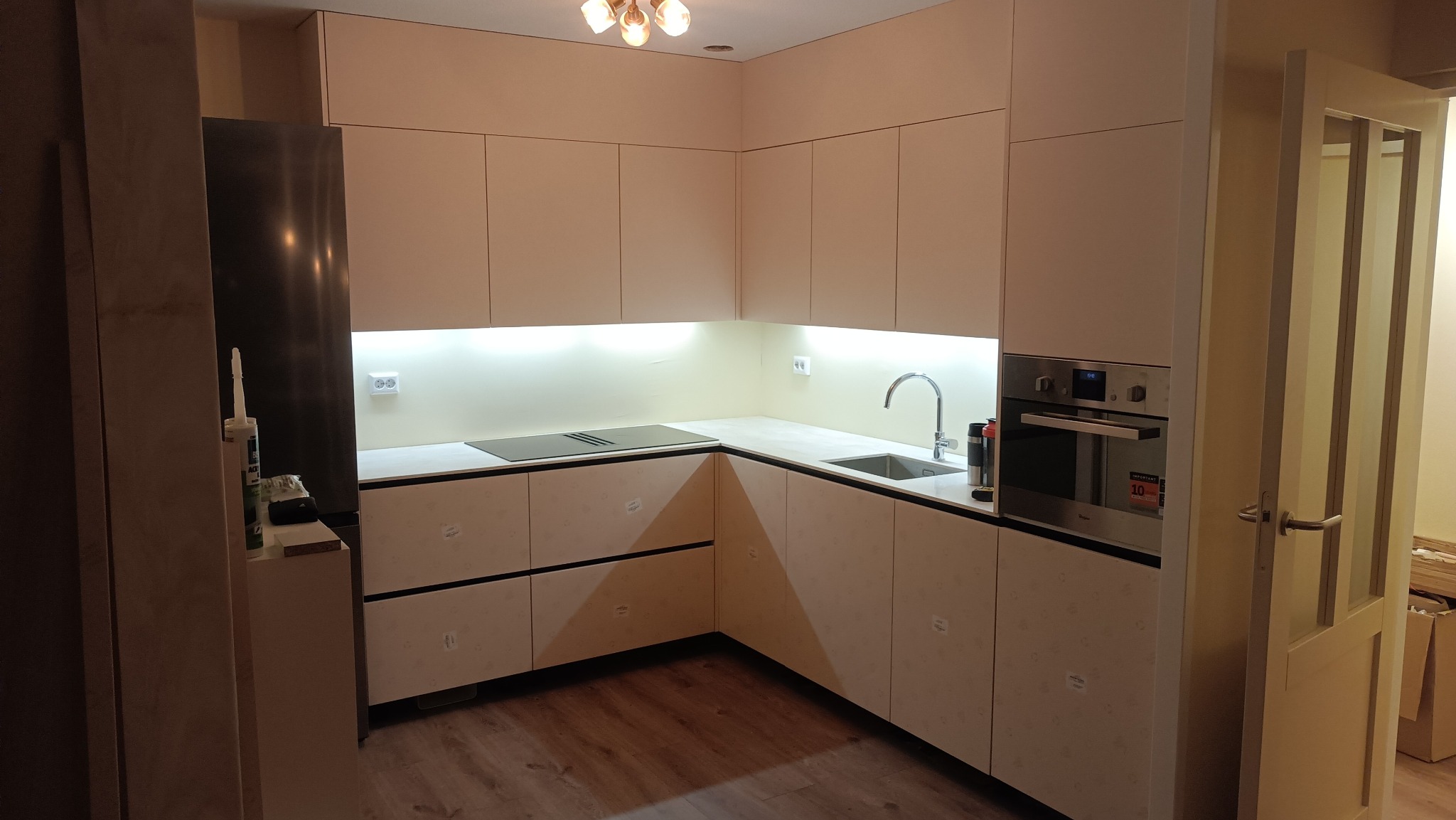 Jasna kuchnia z zabudową pod sufit w Skoczowie. Minimalistyczne fronty szafek dolnych z poziomymi, ciemnymi akcentami. Płyta indukcyjna i piekarnik w zabudowie.