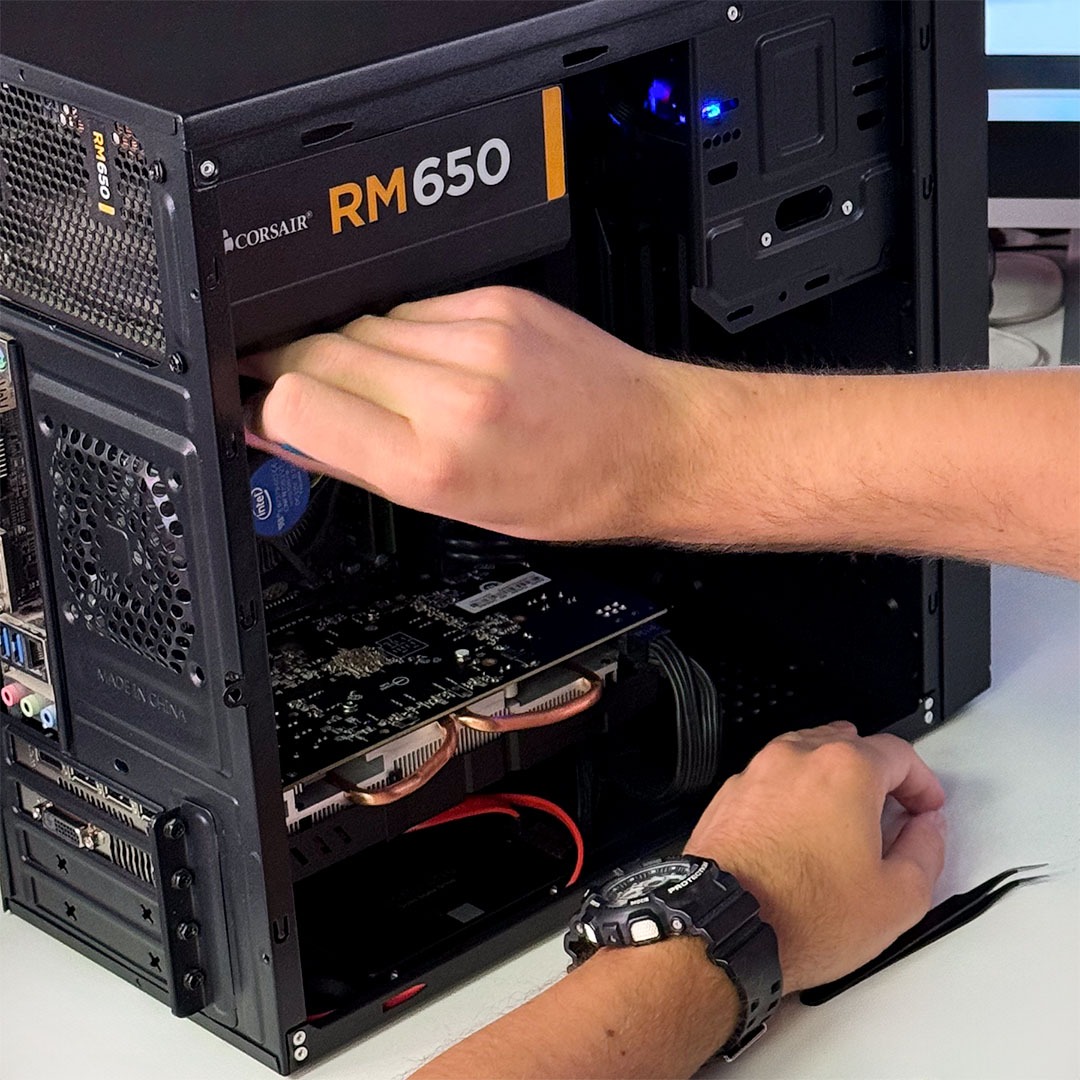 Montaż komputera stacjonarnego: ręce instalują przewody w obudowie z zasilaczem Corsair RM650 i kartą graficzną. Widoczne narzędzia i zegarek na nadgarstku.