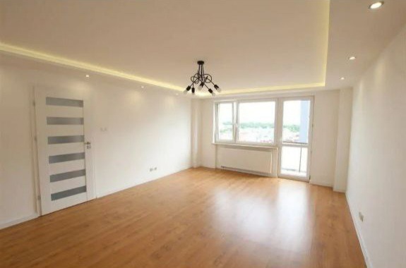 Jasne, przestronne wnętrze po remoncie: parkiet, białe ściany, okno z widokiem, designerska lampa i sufit z oświetleniem punktowym. Minimalistyczny styl.