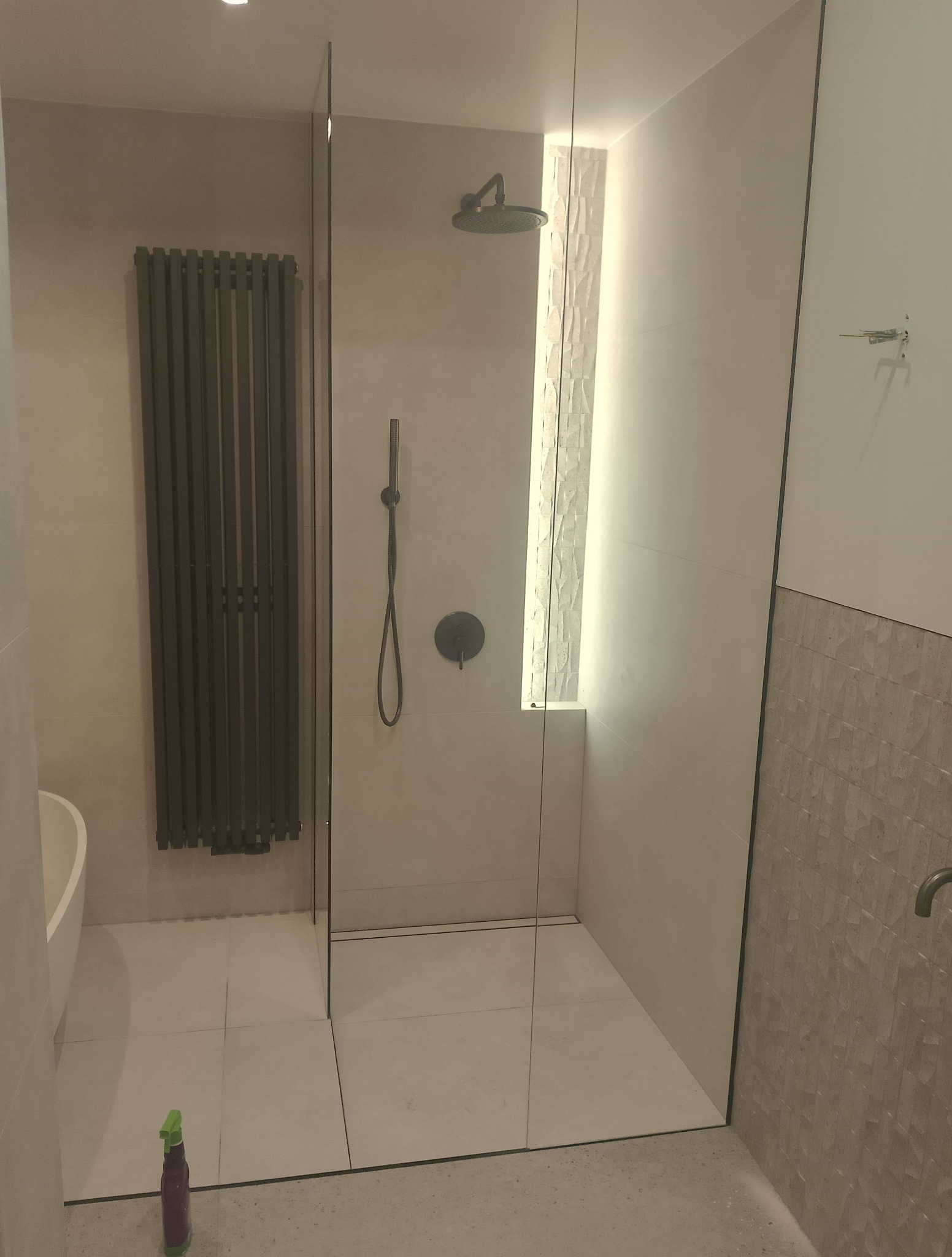 Nowoczesna łazienka z kabiną typu walk-in, grzejnikiem drabinkowym i panelami dekoracyjnymi. Minimalistyczny design, stonowana kolorystyka i oświetlenie LED.