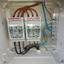 ŁUKASZ STELMACH - Rozdzielnica elektryczna APATOR RBK00 z bezpiecznikami, widoczne okablowanie w kolorach brązowym, niebieskim i żółto-zielonym. Instalacja w białej skrzynce.