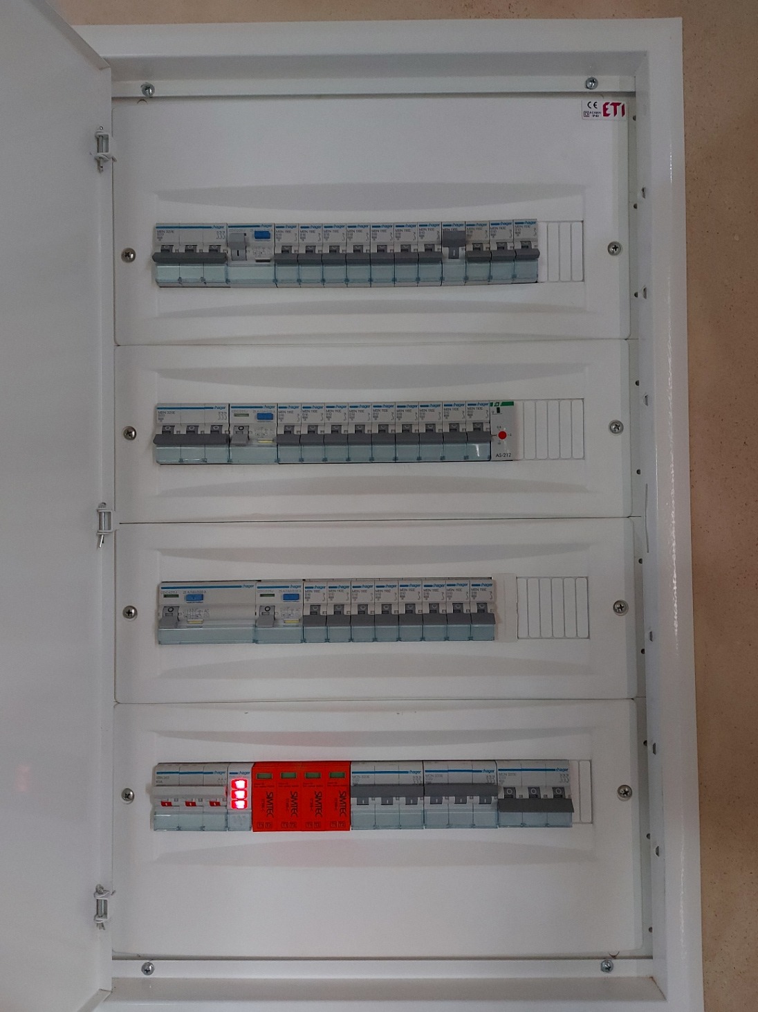 Rozdzielnica elektryczna z bezpiecznikami i zabezpieczeniami przeciwprzepięciowymi, widok z bliska na białą obudowę i zainstalowane komponenty.