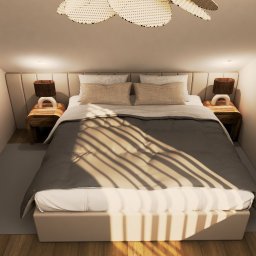 Inspire Design Agata Miroń - Jasna sypialnia na poddaszu z beżowym łóżkiem, drewnianymi szafkami nocnymi i lampkami. Na suficie widoczna pleciona lampa. Promienie światła tworzą wzór na pościeli.