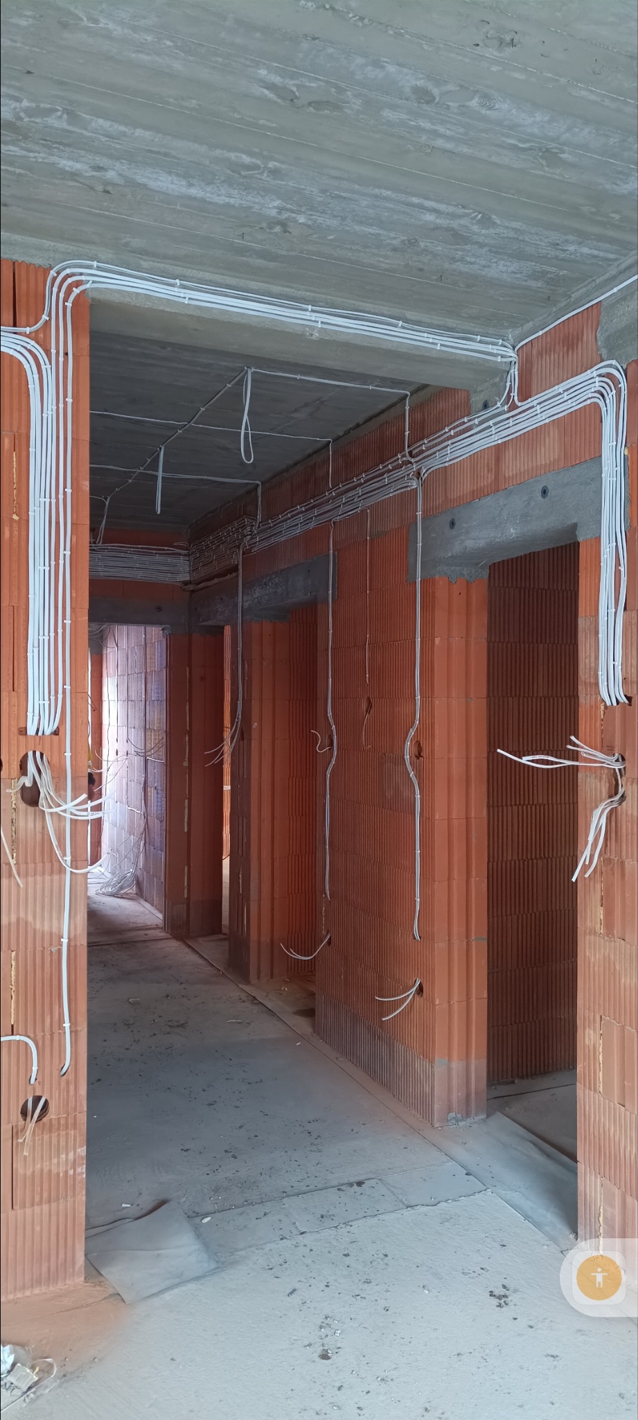 Wnętrze w trakcie prac: widoczne przewody elektryczne ułożone na ścianach z cegły i pod sufitem. Instalacja elektryczna w nowym budynku przed tynkowaniem.