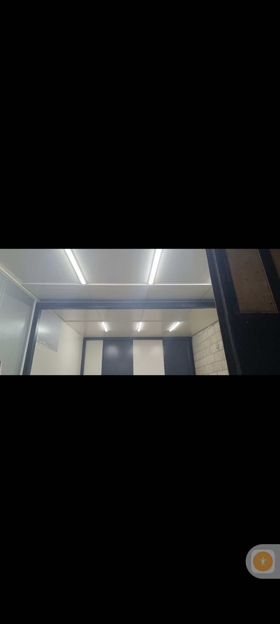 Wnętrze chłodni z panelami w biało-granatowe pasy i oświetleniem jarzeniowym, widziane z zewnątrz przez częściowo otwarte drzwi.