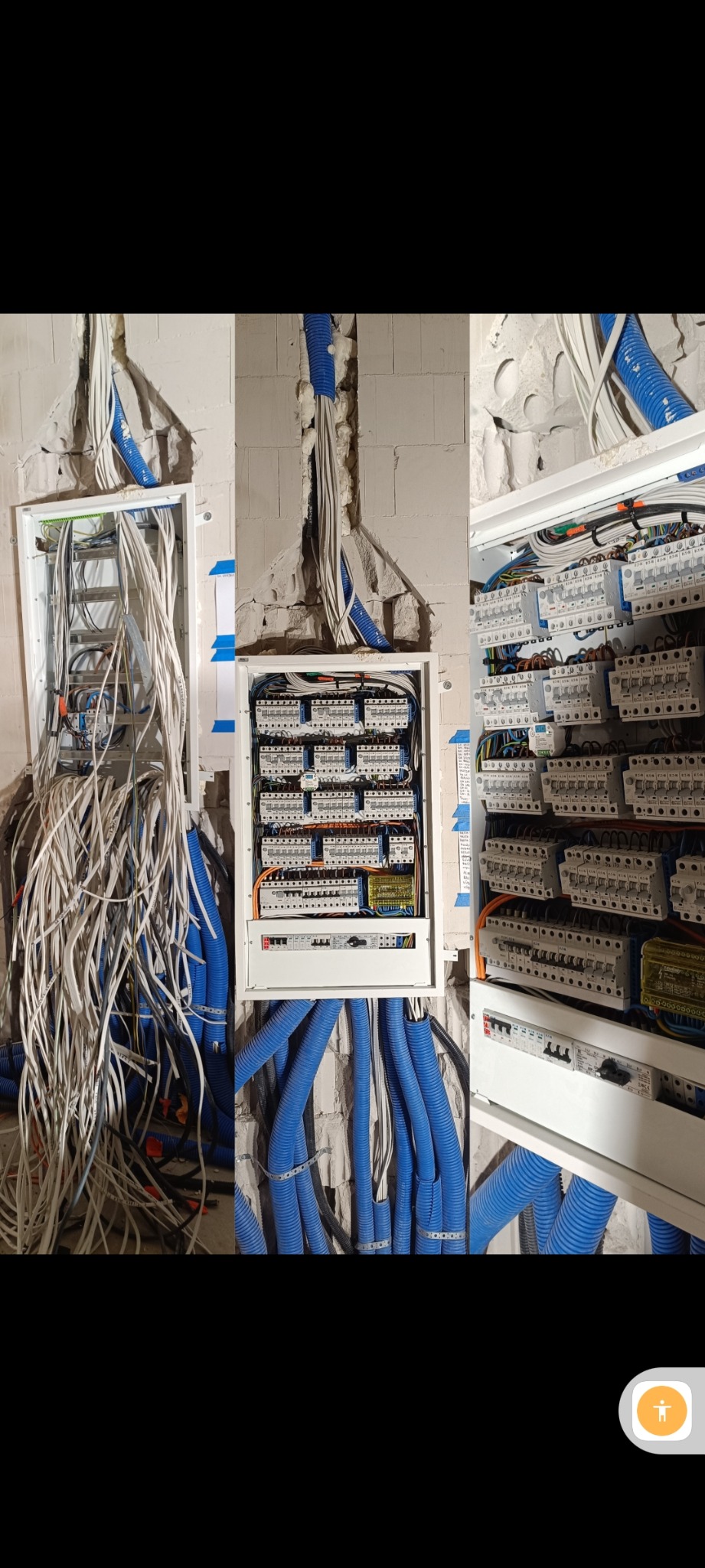 Rozdzielnice elektryczne w trakcie montażu: jedna z chaotyczną wiązką przewodów, druga częściowo uporządkowana, trzecia z kompletnym okablowaniem. Nieotynkowane ściany.