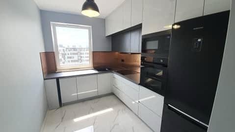 Nowoczesna kuchnia z białymi szafkami i czarnym sprzętem AGD, miedziane panele nad blatem, marmurowe płytki podłogowe, oświetlenie punktowe.