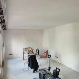 Renovation & Construction Zbigniew Bogdan - Wnętrze w trakcie remontu: świeżo wyszpachlowane ściany, widoczne narzędzia, skrzynki narzędziowe, stół z akcesoriami, przygotowane do dalszych prac wykończeniowych.