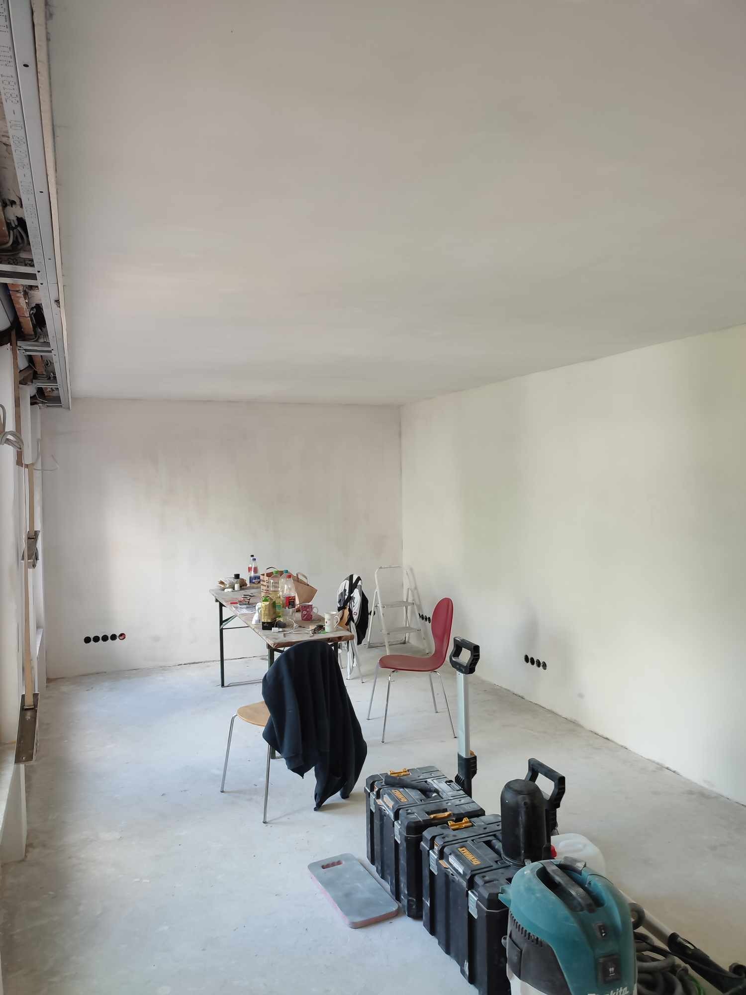 Wnętrze w trakcie remontu: świeżo wyszpachlowane ściany, widoczne narzędzia, skrzynki narzędziowe, stół z akcesoriami, przygotowane do dalszych prac wykończeniowych.