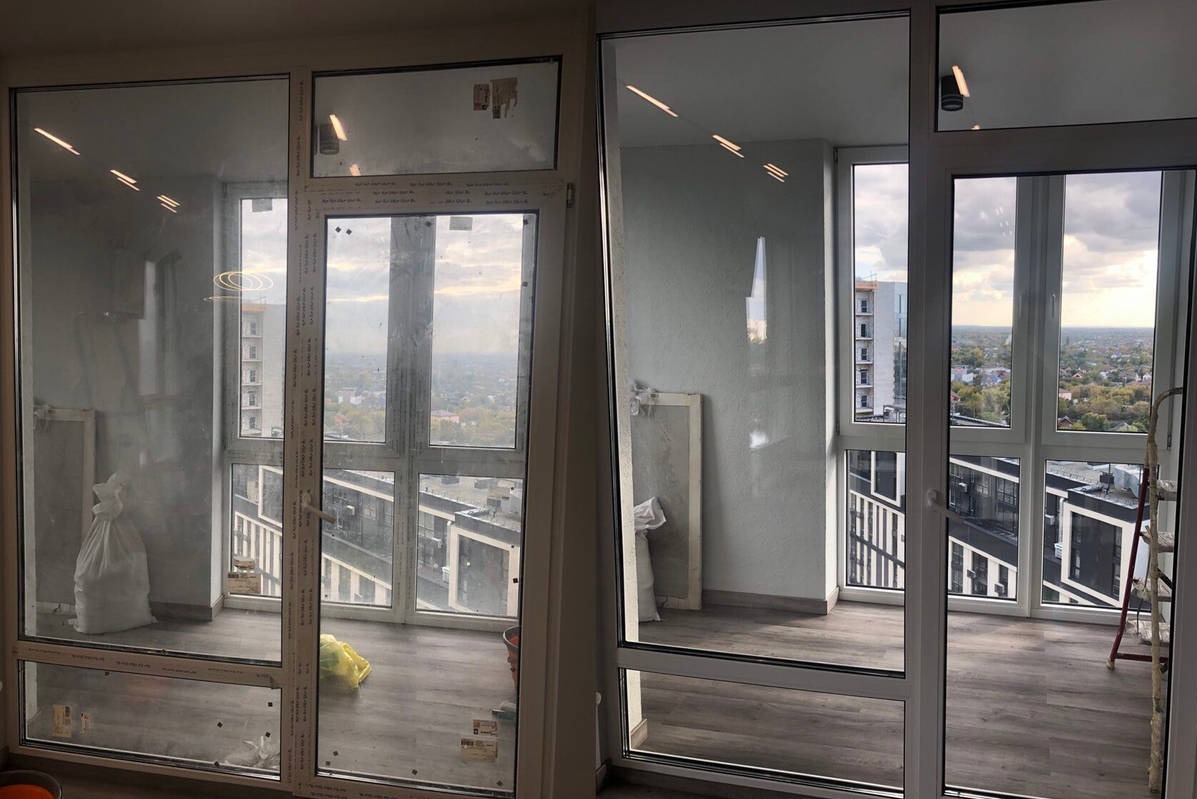 Balkon przed i po czyszczeniu: po lewej stronie brudne szyby, po prawej czyste, z widokiem na miasto. Widoczny fragment drabiny i worki z odpadami.