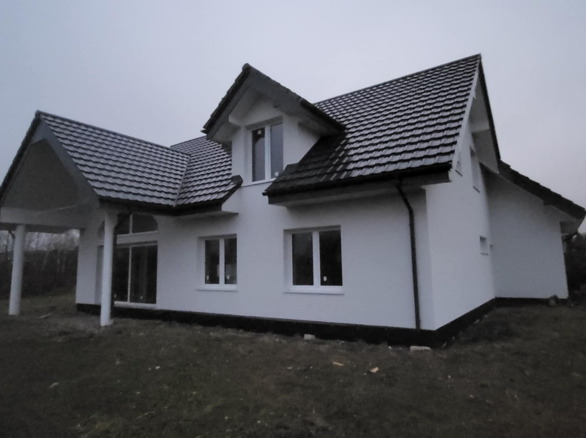 Nowoczesny dom jednorodzinny z białą elewacją i ciemną dachówką w Liniewie, widok z zewnątrz. Minimalistyczny styl, duże okna, spokojna kolorystyka.