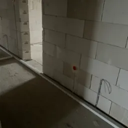 Wnętrze w trakcie prac: ściany z betonu komórkowego, białe listwy przypodłogowe, wystające przewody elektryczne z czerwonym gniazdkiem w ścianie.