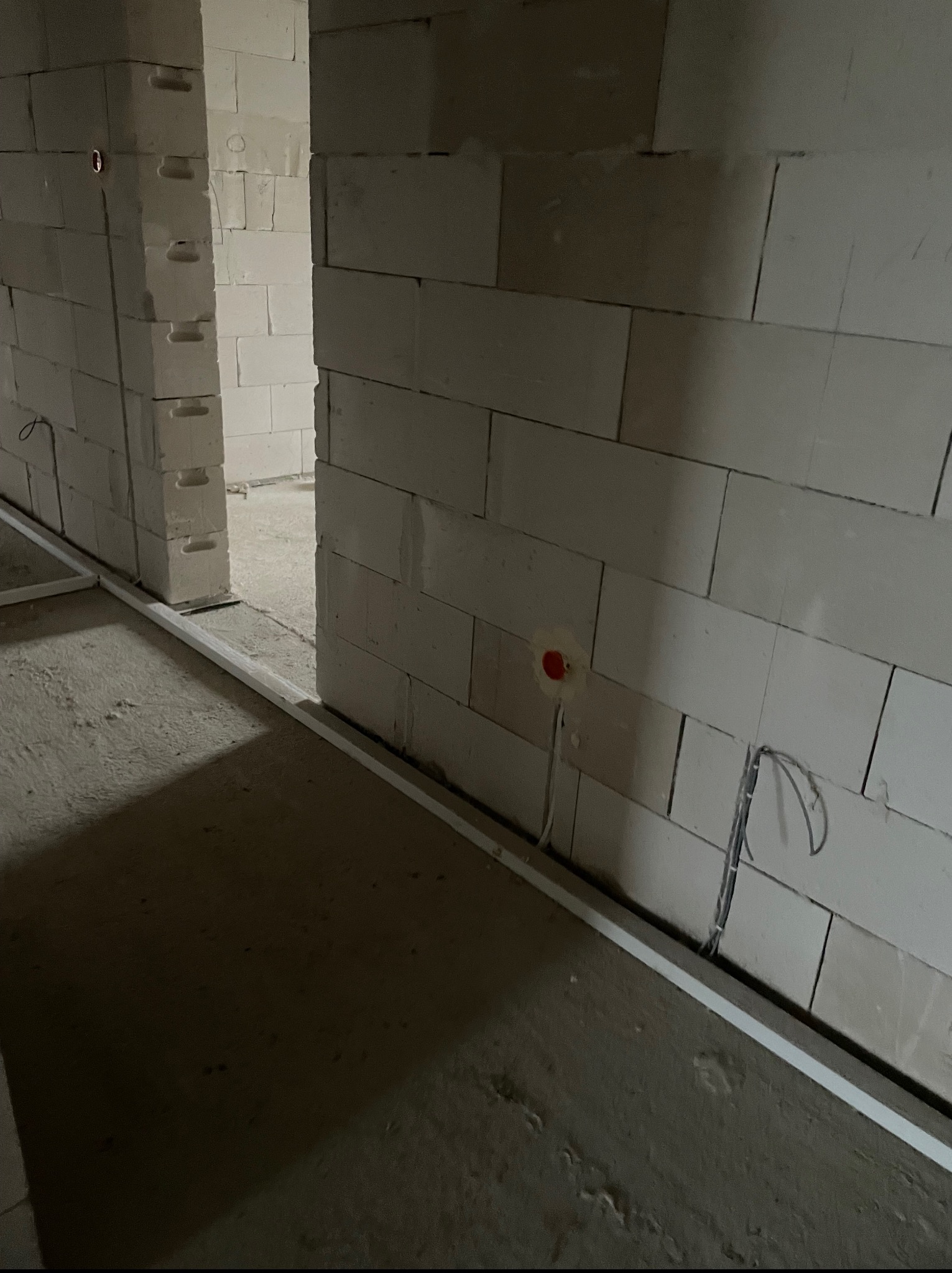 Wnętrze w trakcie prac: ściany z betonu komórkowego, białe listwy przypodłogowe, wystające przewody elektryczne z czerwonym gniazdkiem w ścianie.