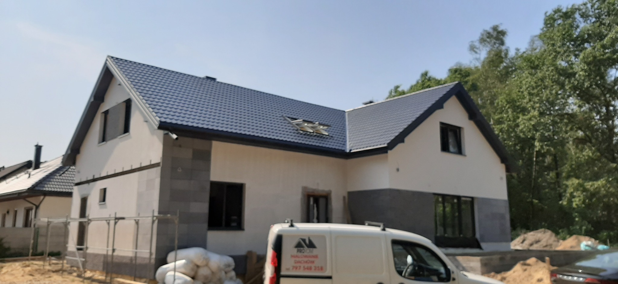 Dom z nowym, grafitowym dachem i fragmentem elewacji w trakcie wykończenia. Na pierwszym planie samochód dostawczy z logo firmy dekarskiej.