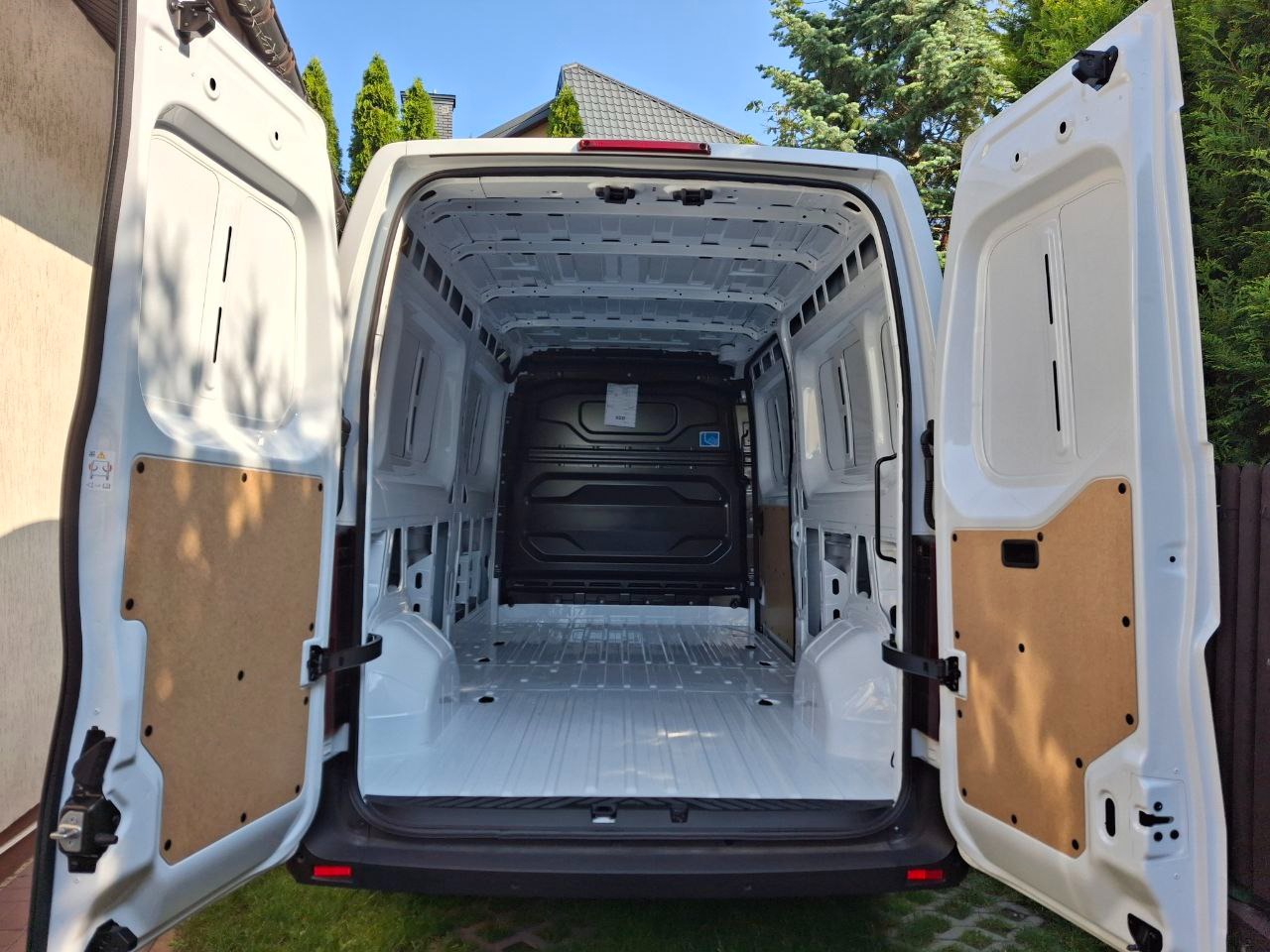 Wnętrze białego, pustego busa z otwartymi tylnymi drzwiami, gotowego do załadunku. Widoczna czysta podłoga i ściany, sugerujące przygotowanie do transportu.