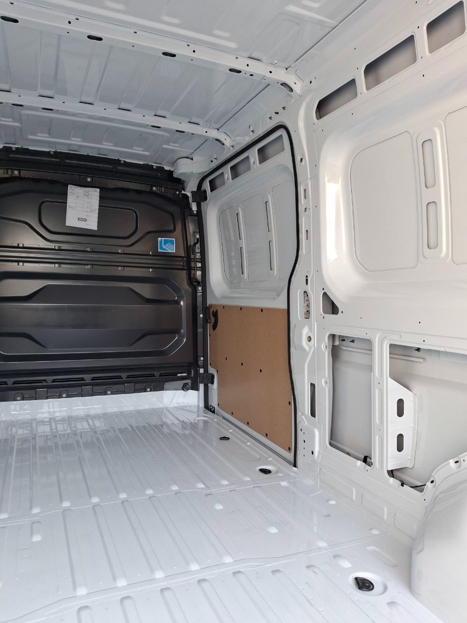 Wnętrze czystego, białego furgonetki z metalową podłogą i ścianami. Widoczne elementy konstrukcyjne i zabezpieczenia ścian. Przygotowany do transportu towarów.