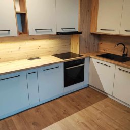 GraStol - Jasna kuchnia z drewnianymi akcentami: fronty w odcieniach błękitu i beżu, czarne uchwyty i armatura, drewniany blat i panel ścienny. Nowoczesny design.