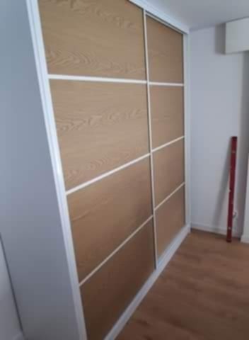 Wnętrze z dużą, przesuwną szafą wnękową. Drzwi z paneli w odcieniach drewna, obramowane białymi listwami. Podłoga drewniana. Minimalistyczny design.