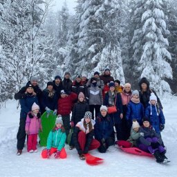 Invictus Przemysław Gałaszewski - Grupa ludzi z sankami w zimowym lesie, prawdopodobnie uczestnicy wycieczki lub obozu zimowego. Śnieżne drzewa w tle, pochmurne niebo.