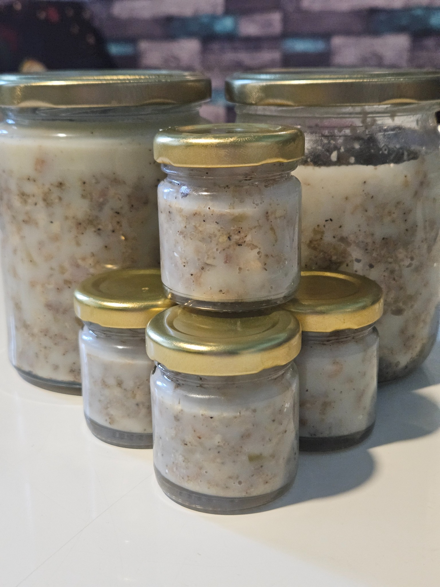 Domowy smalec w słoikach z zakrętkami w odcieniach złota, różnej wielkości. Dwa duże słoiki z tyłu i piramida z trzech małych z przodu.