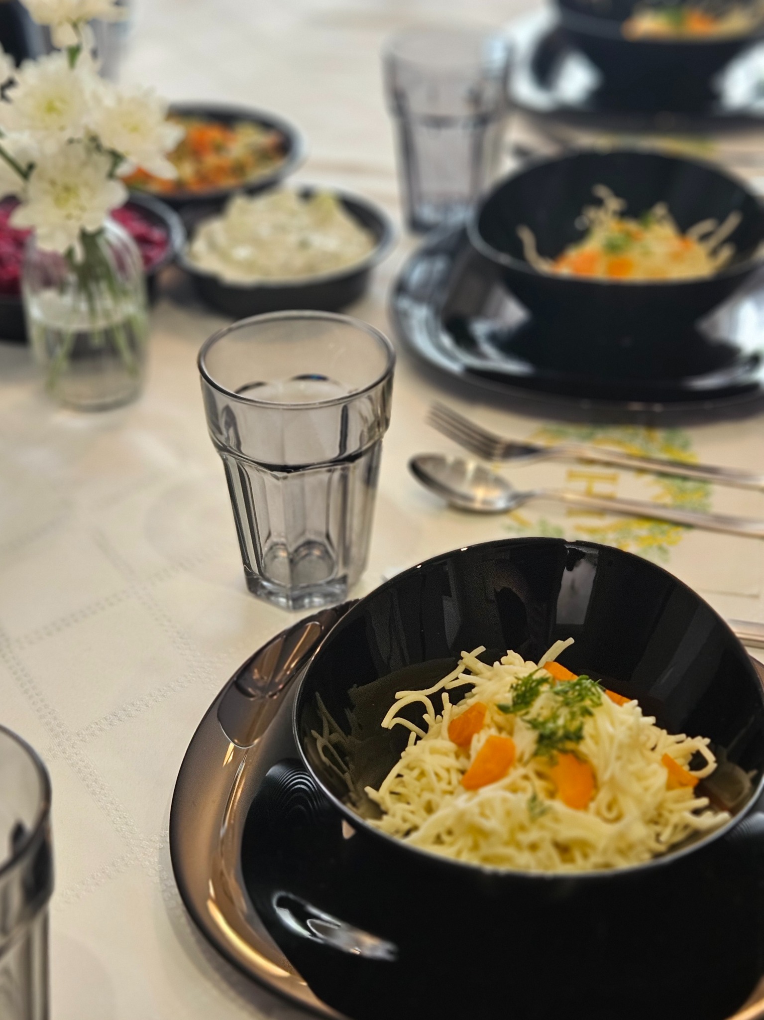 Elegancko nakryty stół z czarnymi miseczkami z sałatką, szklankami i kwiatami w wazonie, tworzący wyrafinowaną kompozycję cateringową.