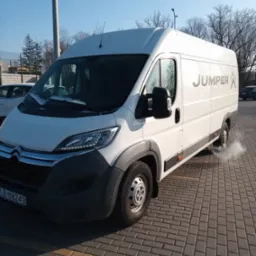 Biały bus marki Citroen Jumper na brukowanym parkingu w słoneczny dzień. Widoczne logo Jumper na boku pojazdu i tablica rejestracyjna. Minimalna ilość śniegu na masce.