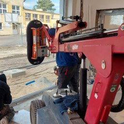 AKO - Montaż okna z użyciem specjalistycznego podnośnika UPLIFTER, pracownik w trakcie uszczelniania ramy, widoczne profile okienne ALLUPROF.