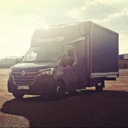 CC.Transport Międzynarodowy - Czarny bus dostawczy Renault Master z zabudową skrzyniową na placu portowym, w tle kontenery, żurawie i budynki przemysłowe, słoneczny dzień.