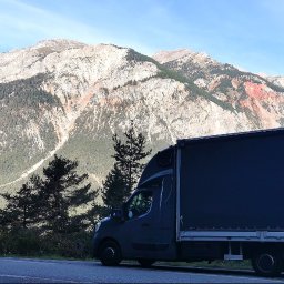 CC.Transport Międzynarodowy - Czarny bus dostawczy na tle malowniczego górskiego krajobrazu z drzewami. Widok z boku, oświetlenie naturalne.